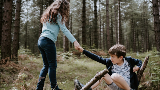 Girl helping boy up from the ground in the woods - photo credit @anniespratt