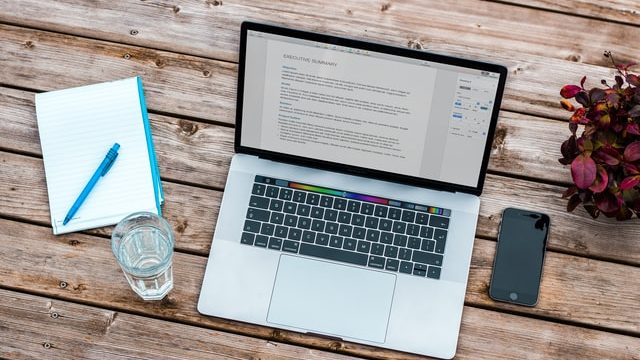 Find a co-op job in Canada - Laptop showing Resume with photo, notebook water and plan on wooden table - shot from above. Photo credit @bramnaus