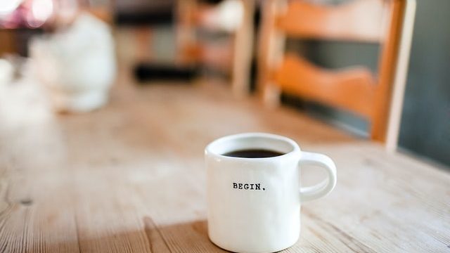 white coffee mug on a table with the with the word "Begin" on it