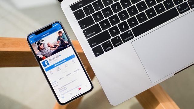 facebook app on mobile phone and corner of mac laptop